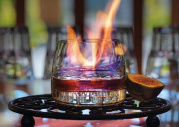 Glas auf gusseisernem Tablett mit etwas Rum und Kaffee befuellt, einer Feige daneben und einer Flamme im Glas