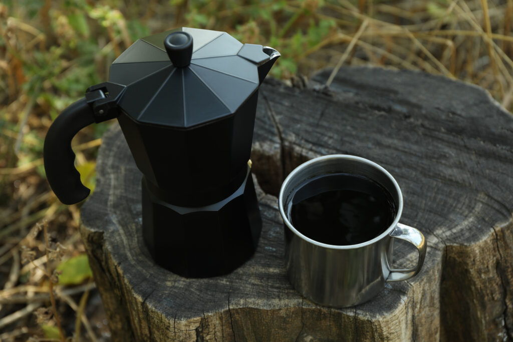 Coffee maker and cup of coffee on stump outdoor