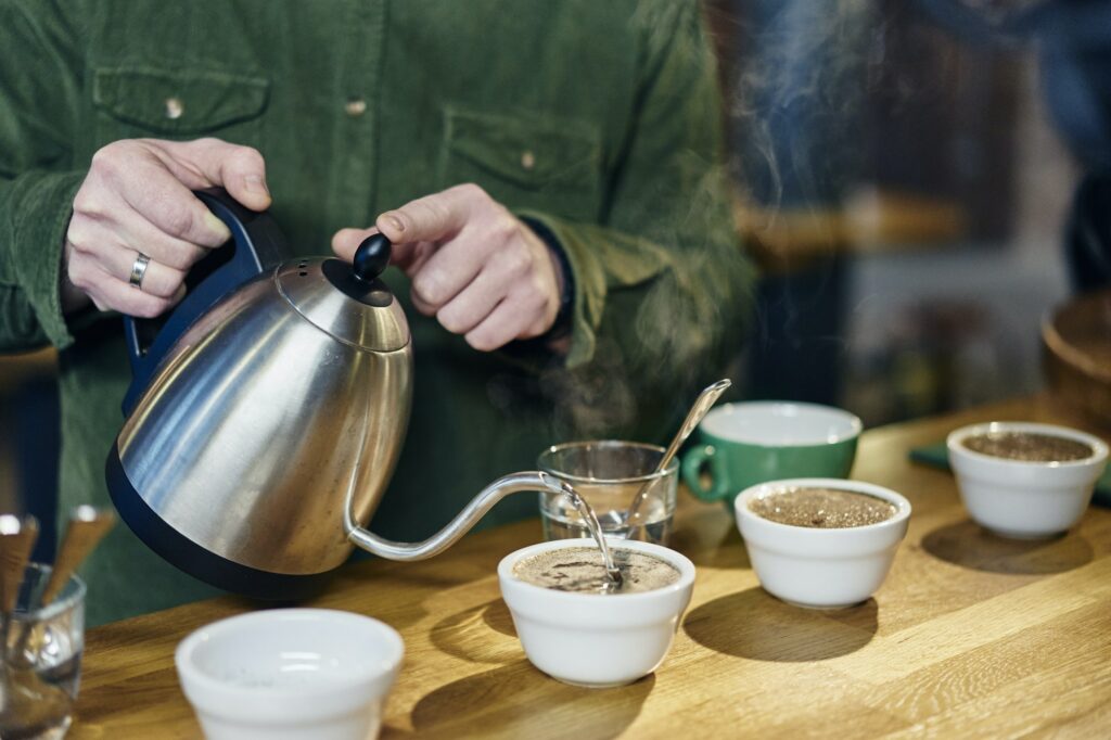 Man pouring boiling water into coffee bowls for tasting on coffee shop counter