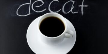 top view black coffee on a black background with inscription decaf made with white chalk