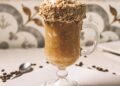 Vertical closeup shot of a barista pouring nuts on a gourmet latte