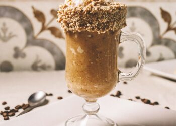 Vertical closeup shot of a barista pouring nuts on a gourmet latte