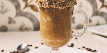 Vertical closeup shot of a barista pouring nuts on a gourmet latte