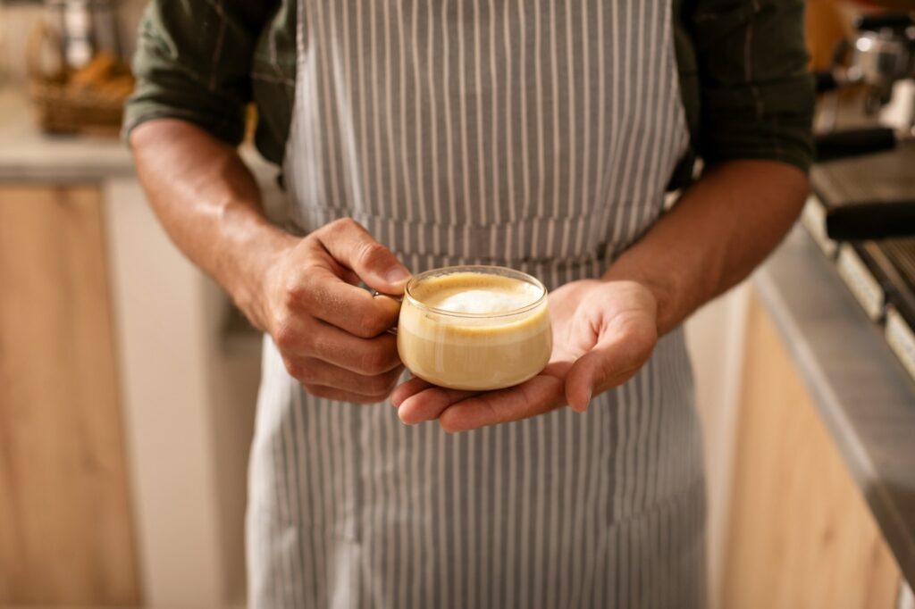 Barista wearing striped apron holding cup of cappuccino