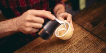 Milchaufschäumen ohne Dampf creating latte art by barista - focus in milk foam and coffee. Vintage color filter