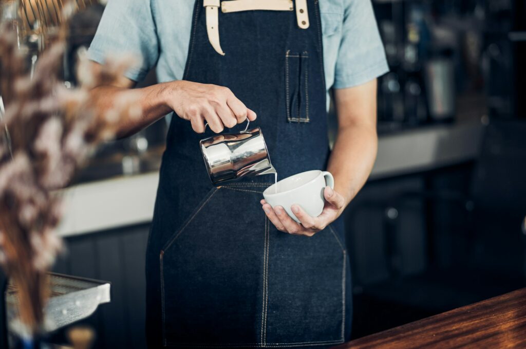 Milchaufschäumen ohne Dampf  Man barista pour milk into hot coffee cup at counter bar