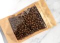 Coffee beans in transparent window pouches on brown paper bags.