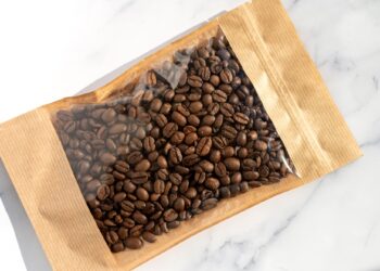 Coffee beans in transparent window pouches on brown paper bags.