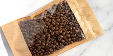 Coffee beans in transparent window pouches on brown paper bags.