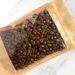 Coffee beans in transparent window pouches on brown paper bags.